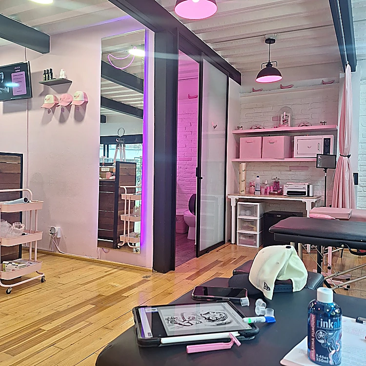 Cabina del estudio con lámpara rosa, repisas rosas, camilla y tableta con un diseño.