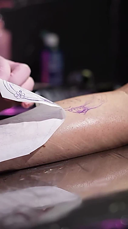 Manos con guantes rosas colocando el papel de transferencia sobre el antebrazo.