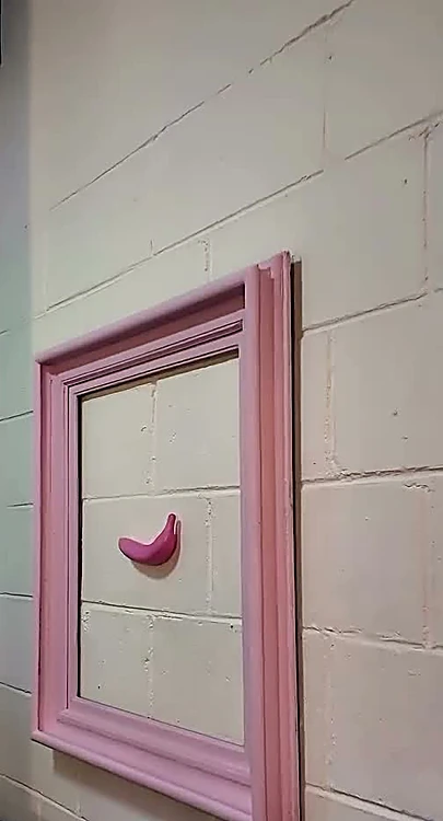 Marco rosa con un plátano rosa colgado en el muro de block blanco del estudio.