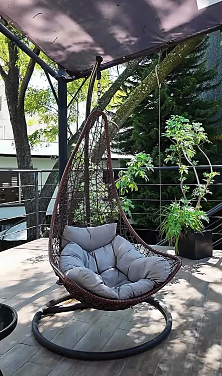 Silla colgante gris en la terraza, entre plantas y bajo un toldo.